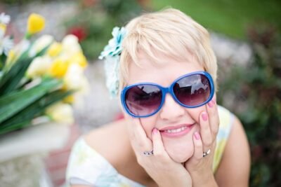 Cheerful Blonde Woman In Her 50s With Sunglasses In Garden